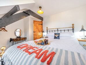 A bedroom with a bed, a wooden door, a mirror, a bedside table, and a hanging light fixture.