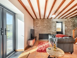 A modern living room with a stone wall, a leather sofa, a glass door leading outside, and a fireplace.