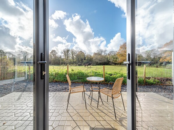 A patio with a table and two chairs, a view of a grassy field, and a fence.
