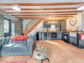 Una cocina moderna con armarios grises, una escalera de madera, un sofá gris con una manta roja y un piso de baldosas.