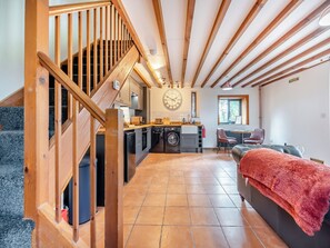 Una cocina amplia con una isla central, un comedor con mesa y sillas, una sala de estar con sofá, y una escalera de madera que sube a otro nivel.