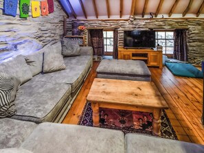 A cozy living room with a stone wall, a sofa set, a wooden coffee table, and a television.