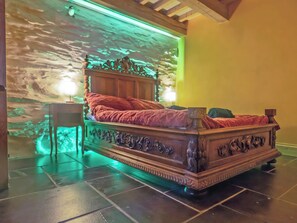 A bed with ornate carvings, a nightstand, and a wall with a green light.
