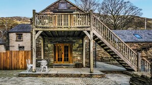 A rustic stone building with a wooden balcony and a staircase leading to a second floor. - 4 bedroom accommodation in Betws Garmon, near Beddgelert (Betws Garmon, near Beddgelert)