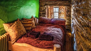 A rustic wooden bed in a stone-walled room with a green wall and a window with curtains. - 4 bedroom accommodation in Betws Garmon, near Beddgelert (Betws Garmon, near Beddgelert)