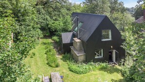 Une maison moderne avec un toit en pente, une cheminée en pierre et un petit patio agrémenté d’une table et de chaises.