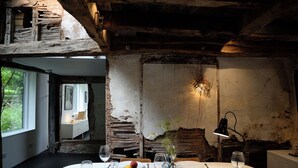 Une salle à manger rustique avec un plafond en bois, une table dressée pour deux personnes, avec des assiettes, des verres et un panier de fruits.