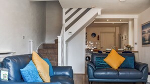 Ein Wohnzimmer mit zwei blauen Ledersofas, einem blauen Teppich und einer Treppe, die in einen Küchenbereich führt.
