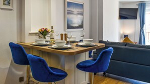 Ein Essbereich mit einem Holztisch, gedeckter für vier Personen, blauen Stühlen, einer Couch und einem Gemälde an der Wand.