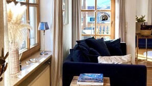 En hyggelig stue med en mørkeblå sofa, et træbord og et vindue med gardiner.