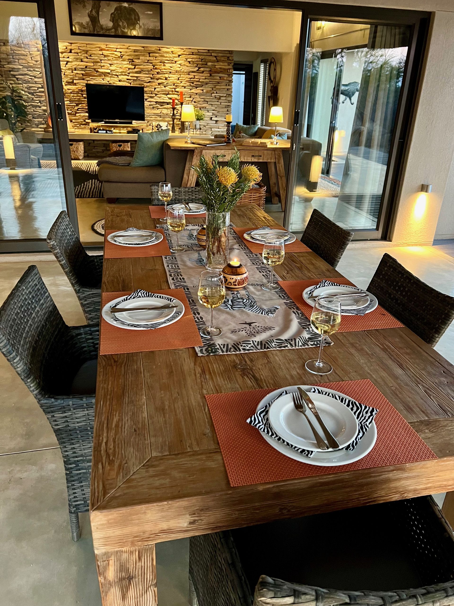 Une table à manger dressée avec des assiettes, des couverts et des verres, et un vase de fleurs et des bougies placés au centre.