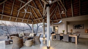 A spacious outdoor seating area with a thatched roof, wicker furniture, and a view of the surrounding landscape. - Villa Marula: Delightful South African bush villa (Hoedspruit)