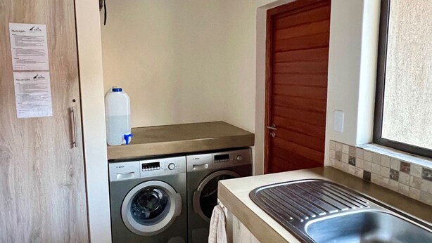 A compact kitchen with a washing machine, a sink, and a wooden door. - Villa Marula: Delightful South African bush villa (Hoedspruit)
