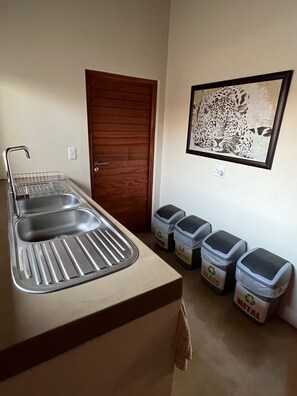 A kitchenette with a double sink, a wooden door, and recycling bins labeled 'paper,' 'glass,' and 'metal.'