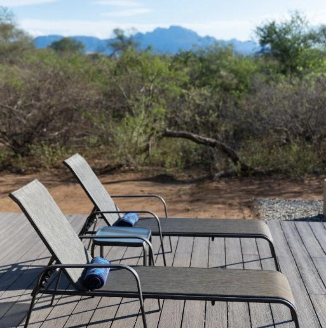 A wooden deck with metal chairs, a blue towel, and a view of a mountainous landscape.