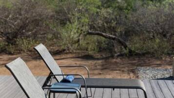 A wooden deck with metal chairs, a blue towel, and a view of a mountainous landscape.
