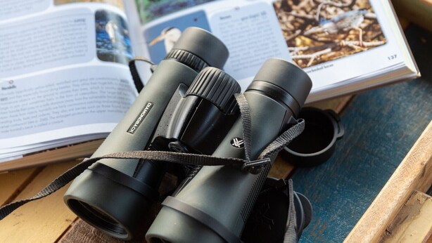 A pair of binoculars on a wooden tray with an open book featuring wildlife photography.