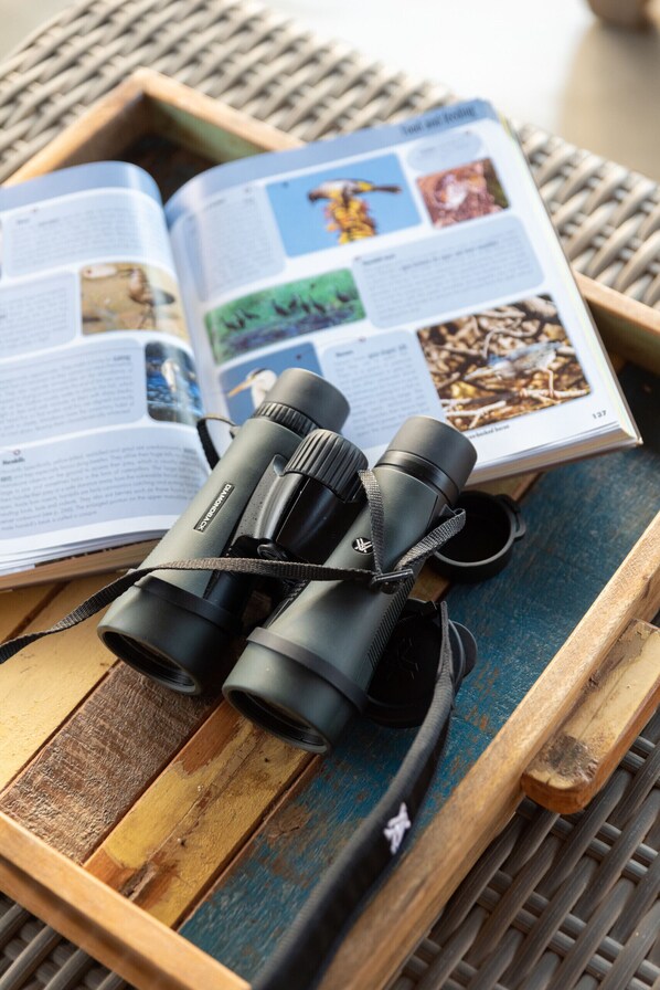 A pair of binoculars on a wooden tray with an open book featuring wildlife photography.