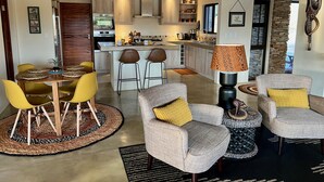 A modern kitchen with a central island, bar stools, and a dining table with yellow chairs. - Villa Marula: Delightful South African bush villa (Hoedspruit)