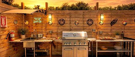 An outdoor kitchen with a grill, sink, and bar area, surrounded by wooden walls and decorative plates.