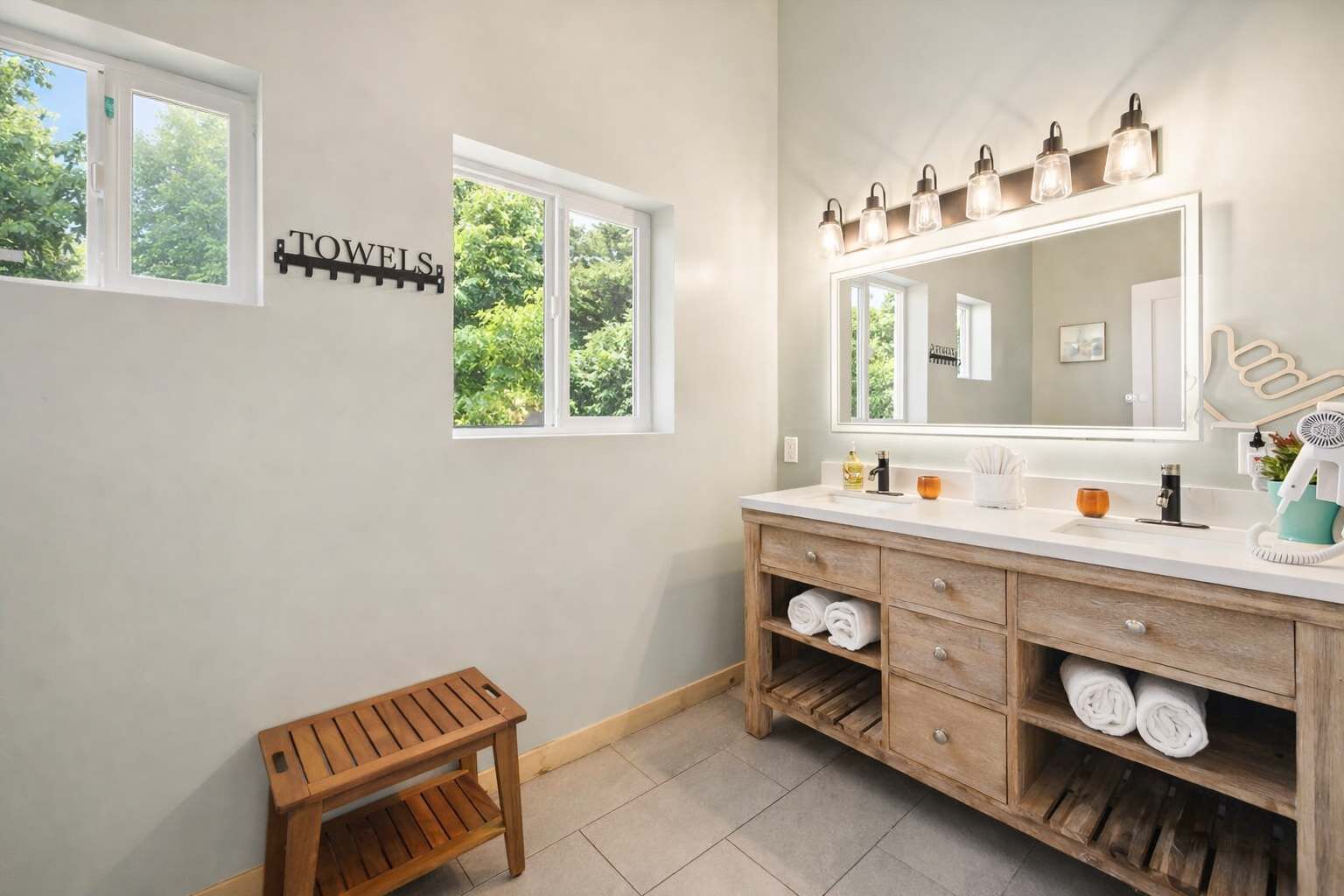 Une salle de bain avec un meuble-lavabo en bois, un grand miroir et un porte-serviettes sur lequel est inscrit le mot « SERVIETTES ».