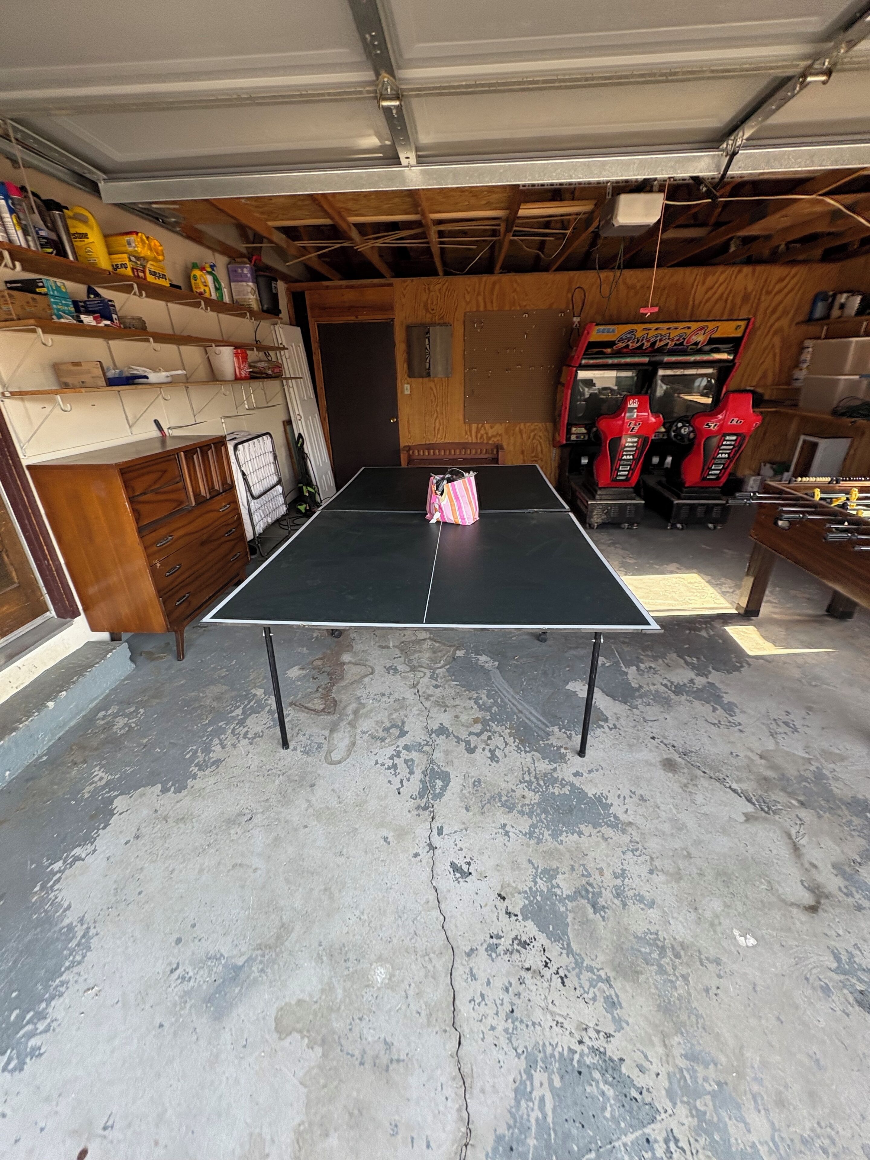 Un garaje con mesa de ping pong, estantes de madera y juegos de arcade.