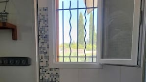 Une salle de bain dotée d’une fenêtre avec une grille en métal, de murs carrelés ornés d’un motif en mosaïque et d’un espace douche.