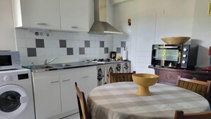 Une cuisine compacte équipée d’un lave-linge, d’un four à micro-ondes et d’un coin repas avec une table et des chaises.