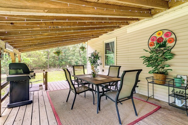 Un patio cubierto con una mesa y sillas de madera, una parrilla y plantas en macetas.