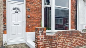 A brick house with a white door, a window, and a small garden area.
