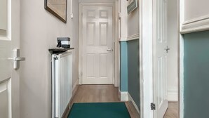 A hallway with a white door, a framed picture above it, a small table with a decorative item, and a green mat at the entrance.