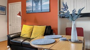 A modern living room with a leather sofa, yellow cushions, a wooden dining table, and a vase with blue flowers.