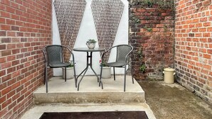 A small outdoor patio with two metal chairs and a round table, surrounded by brick walls and a white fence.
