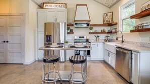 A modern kitchen with white cabinetry, a central island with stools, a stainless steel refrigerator, and a built-in oven. - Recently Built Cabin w/ Pavilion in Granbury! (Granbury)