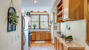 Una cucina con mobili in legno, un frigorifero in acciaio inox, una finestra con vista sugli alberi e una ciotola con palline decorative sul bancone.