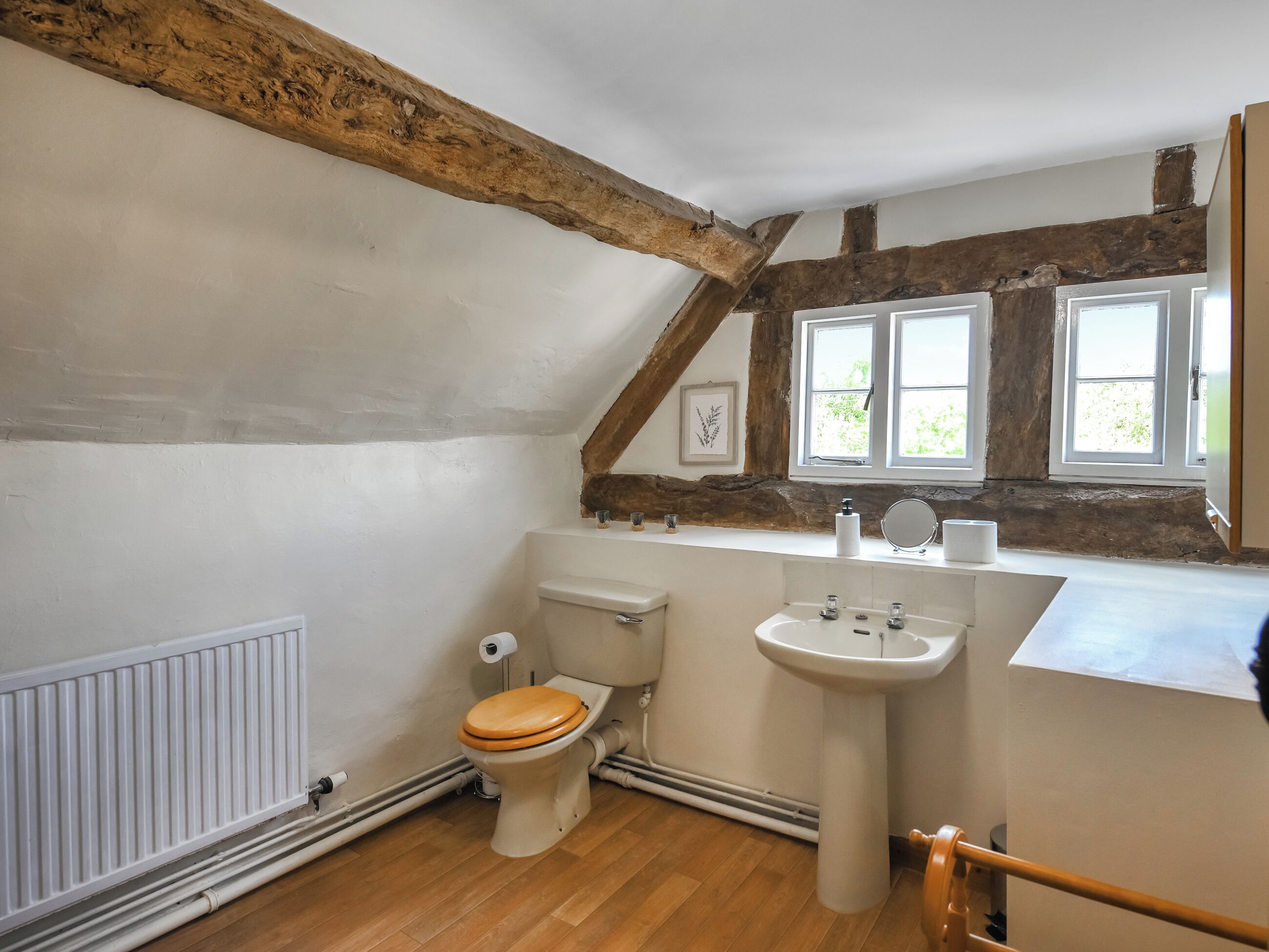 A bathroom with a wooden ceiling, a toilet, a sink, and a window.