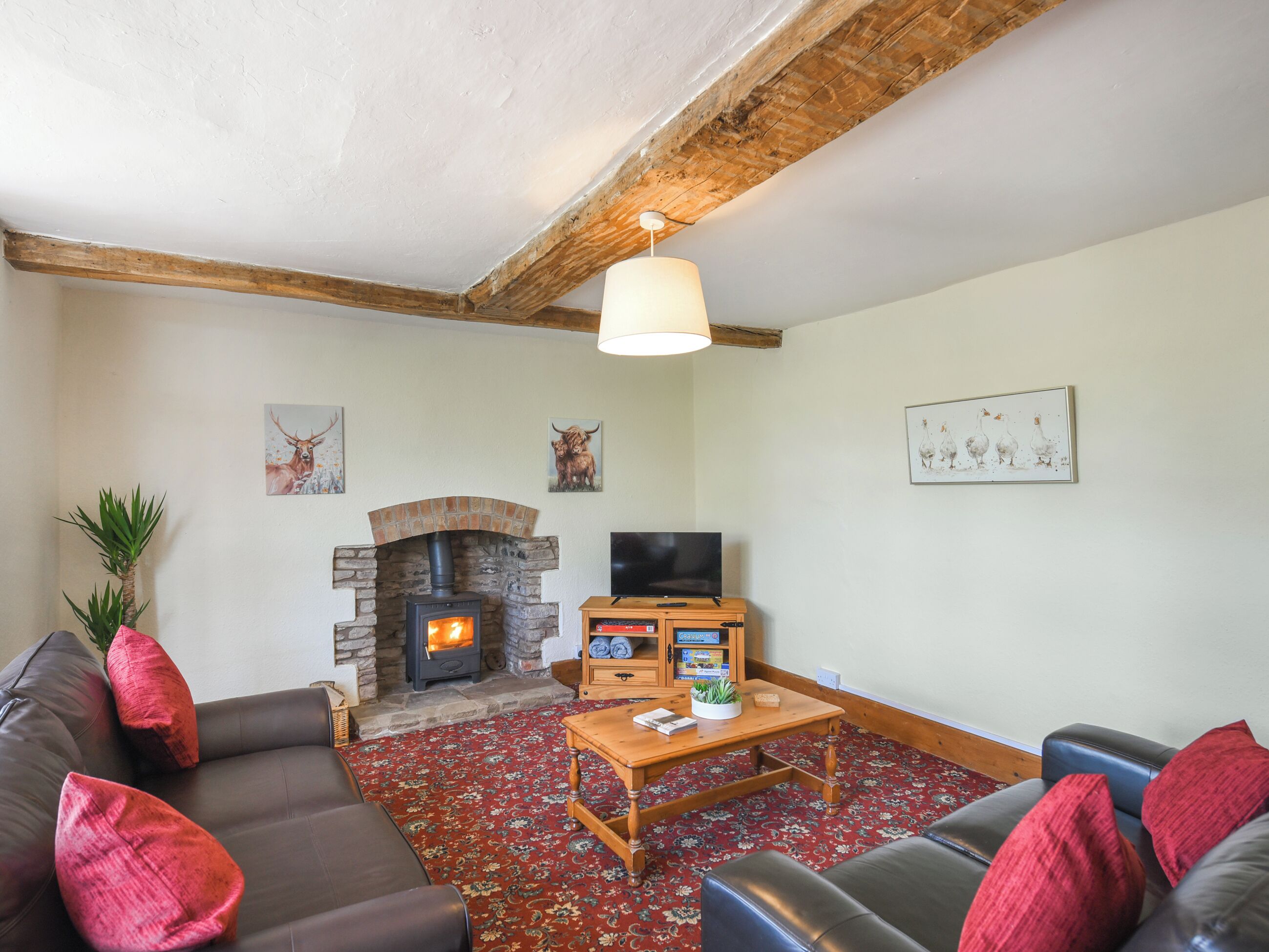 A cozy living room with a stone fireplace, leather sofas, a television, and a red patterned carpet.