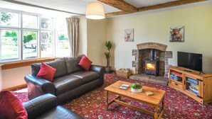 Un salon avec un canapé en cuir, une table basse en bois, une cheminée en pierre et un téléviseur posé sur un meuble en bois.