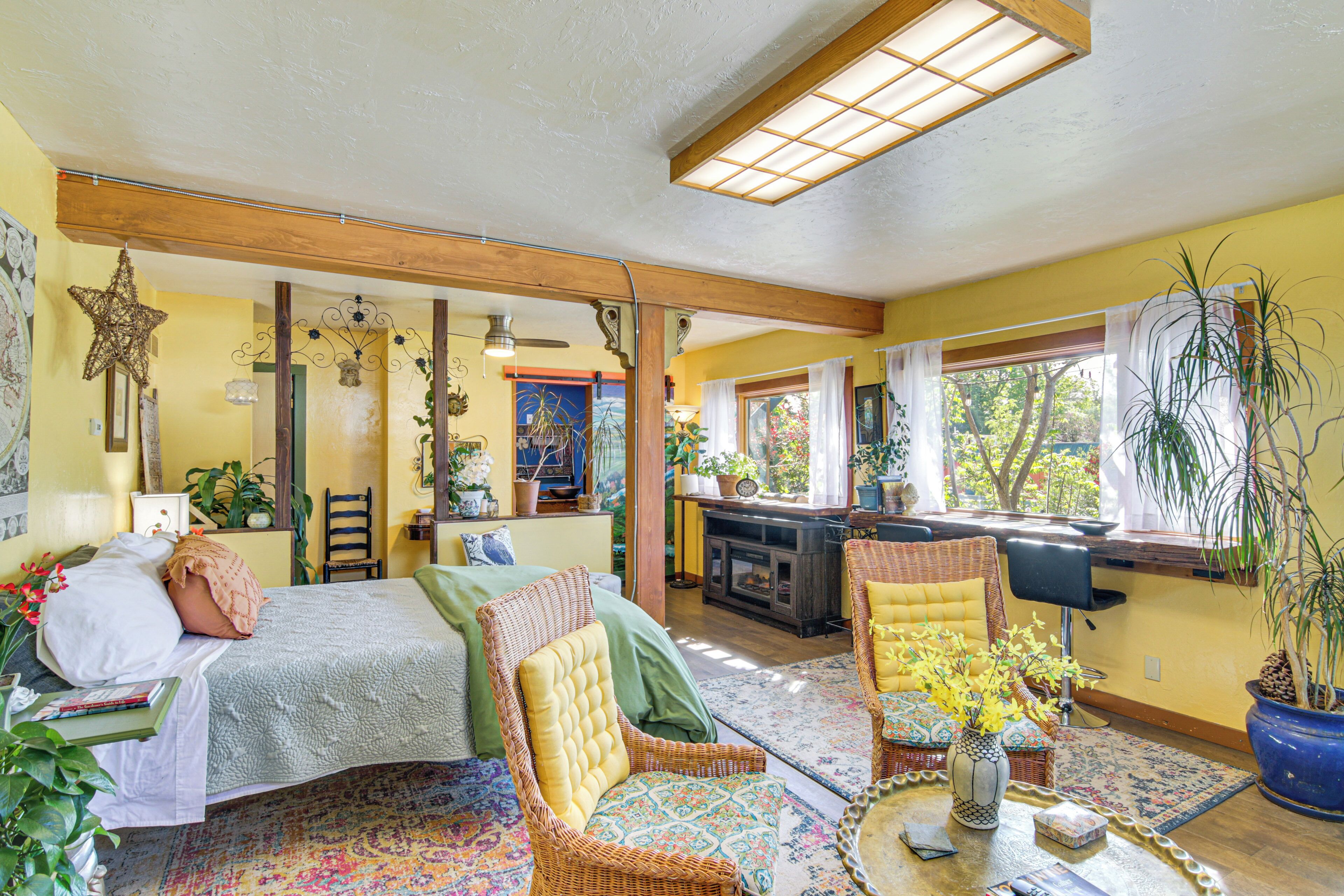 A cozy room with a bed, two chairs, a small table, and a window with plants.