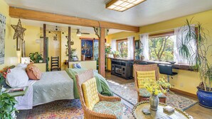 A cozy room with a bed, two chairs, a small table, and a window with plants. - Walk to Dtwn Livingston: Studio w/ Mtn Views! (Livingston)