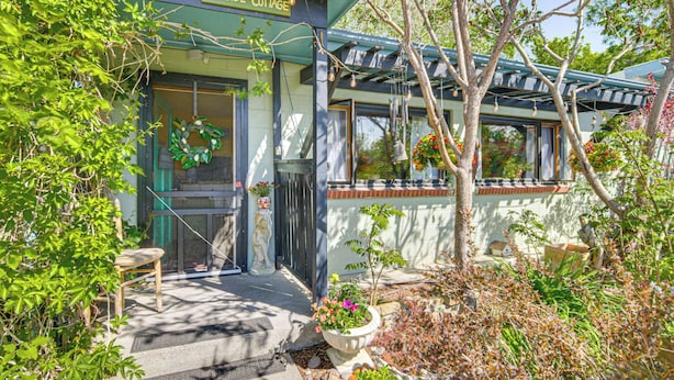 A cozy cottage with a welcoming entrance, a porch with a chair, and a garden area with potted plants and flowers. - Walk to Dtwn Livingston: Studio w/ Mtn Views! (Livingston)