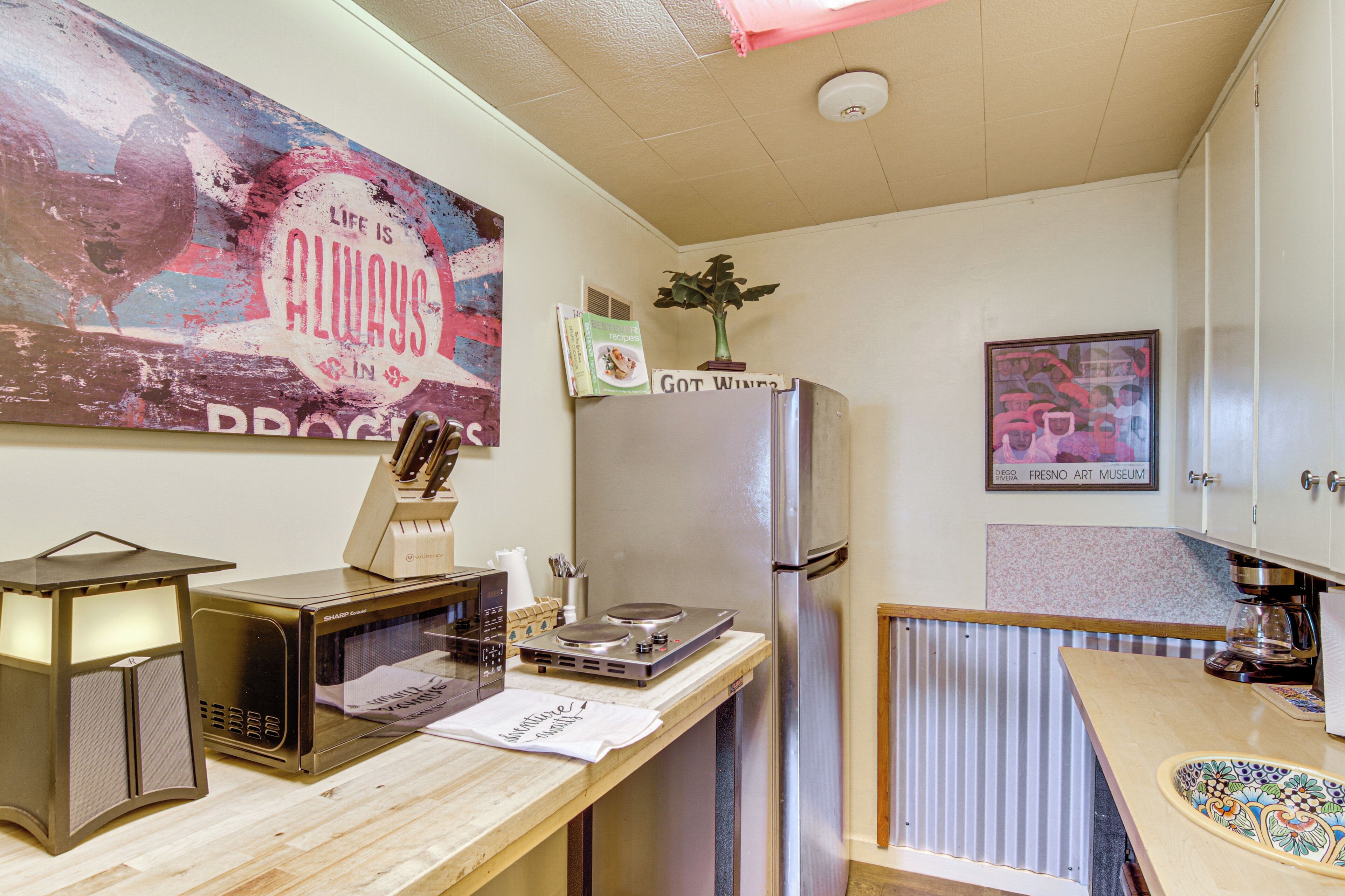 Une cuisine compacte équipée d’un four à micro-ondes, d’un grille-pain et d’un réfrigérateur. On peut voir une affiche accrochée au mur et une photo encadrée d’une voiture.