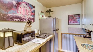 A compact kitchen with a microwave, toaster, and refrigerator. A poster on the wall and a framed picture of a car are visible. - Walk to Dtwn Livingston: Studio w/ Mtn Views! (Livingston)
