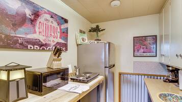 Une cuisine compacte équipée d’un four à micro-ondes, d’un grille-pain et d’un réfrigérateur. On peut voir une affiche accrochée au mur et une photo encadrée d’une voiture.