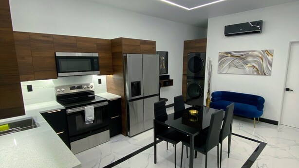 Una cocina moderna con una isla central, electrodomésticos integrados y un comedor con una mesa y sillas negras.
