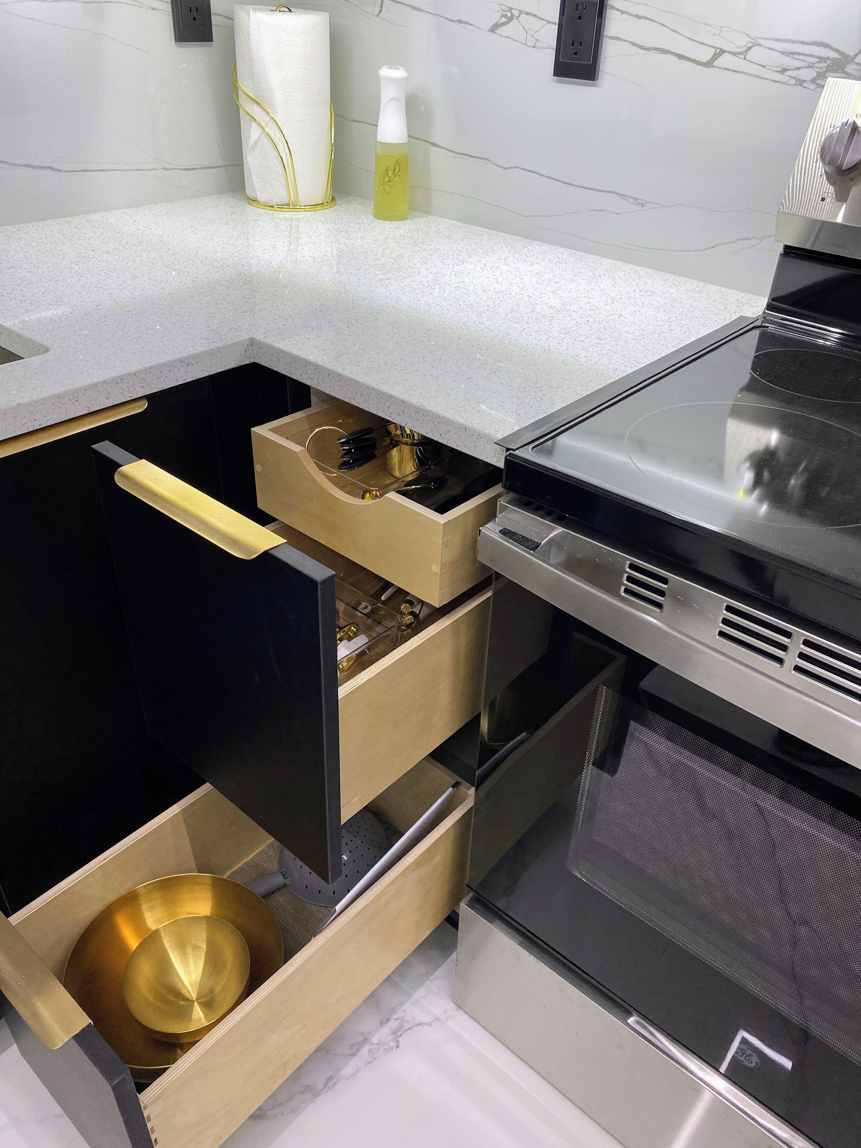 A kitchen with a modern design, featuring a stainless steel stove, a marble countertop, and a gold-colored drawer unit.