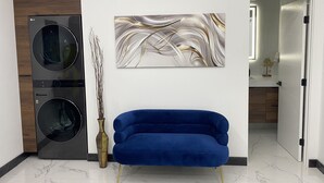 Un moderno lavadero con dos secadoras, un sofá azul, un jarrón decorativo y una obra de arte colgada en la pared.