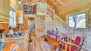 Ein Holzblockhaus-Interieur mit einer Küche, einem Essbereich und einer Treppe, die zu einem Erker führt.