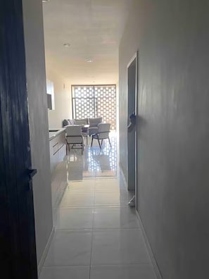 Un couloir mène à une salle à manger équipée d’une table et de chaises, d’une porte coulissante et d’un sol carrelé.