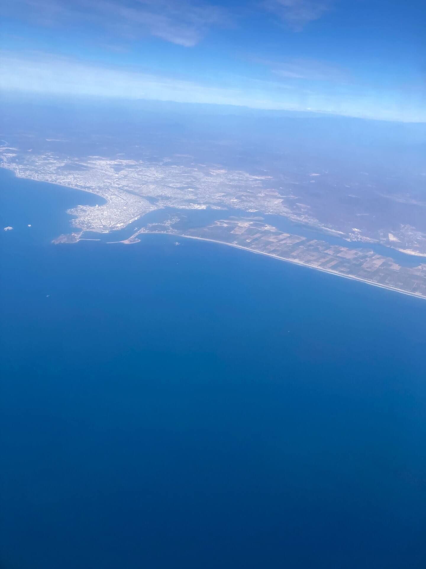 Une vue aérienne d’une ville côtière, avec une mer bleue et limpide, une zone urbaine densément peuplée et une longue étendue de littoral.